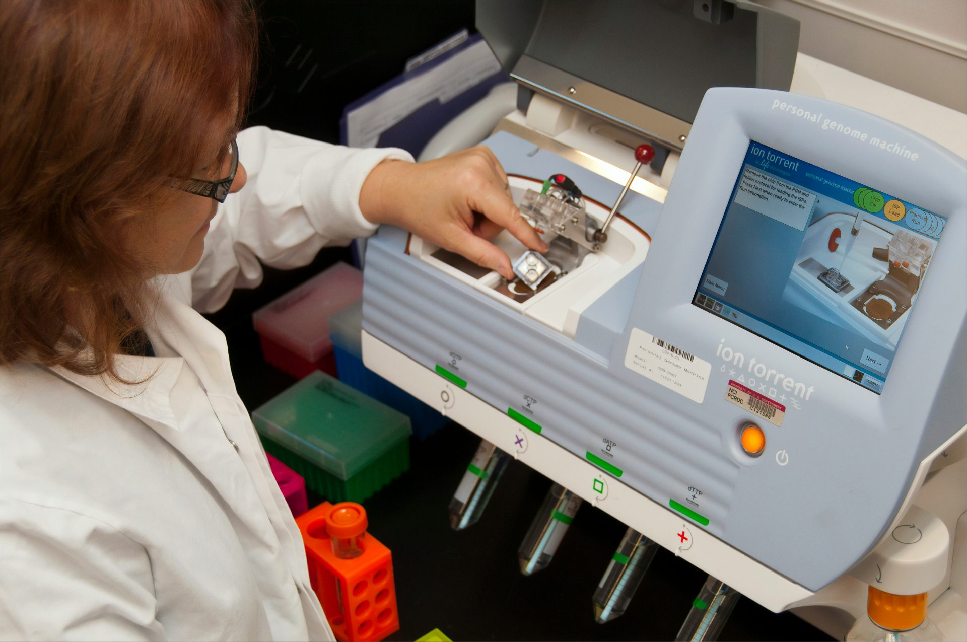 Woman operating laboratory equipment with touchscreen interface.